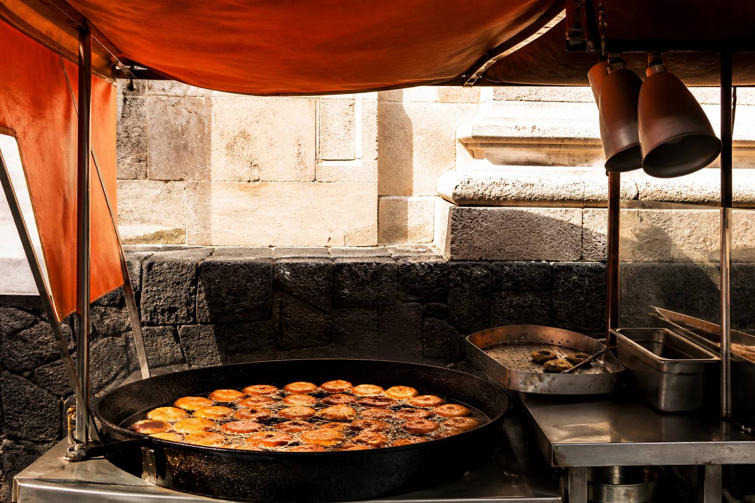 Banco di fritture di strada con padella di panelle sotto una tenda da mercato