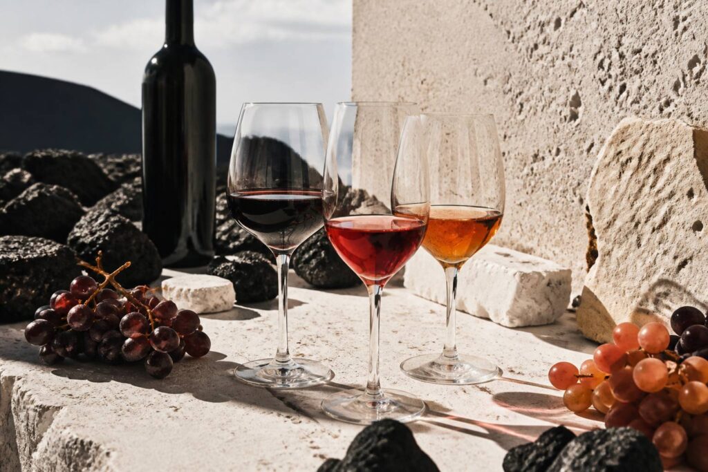 Tre calici di vino siciliano con bottiglia scura e uva su tavola in pietra chiara